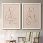 Set of two white barnwood framed canvas prints depicting two minimalist figurative sketches featuring seated female figures drawn with single flowing lines above a sideboard in a cozy sitting room.