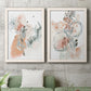 Set of two white barnwood framed canvas prints depicting a coordinated art pair of loose blush gray and coral floral gestures rendered as abstract watercolor botanicals above a sofa in a modern living room.
