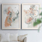 Set of two white barnwood framed canvas prints depicting scribbled petals, translucent washes, and drifting stems arranged across two complementary compositions above a sofa in a bright living space.