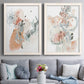 Set of two white barnwood framed canvas prints depicting paired abstract watercolor botanicals with scribbled petals, translucent washes, and drifting stems above a sofa in a contemporary living room.