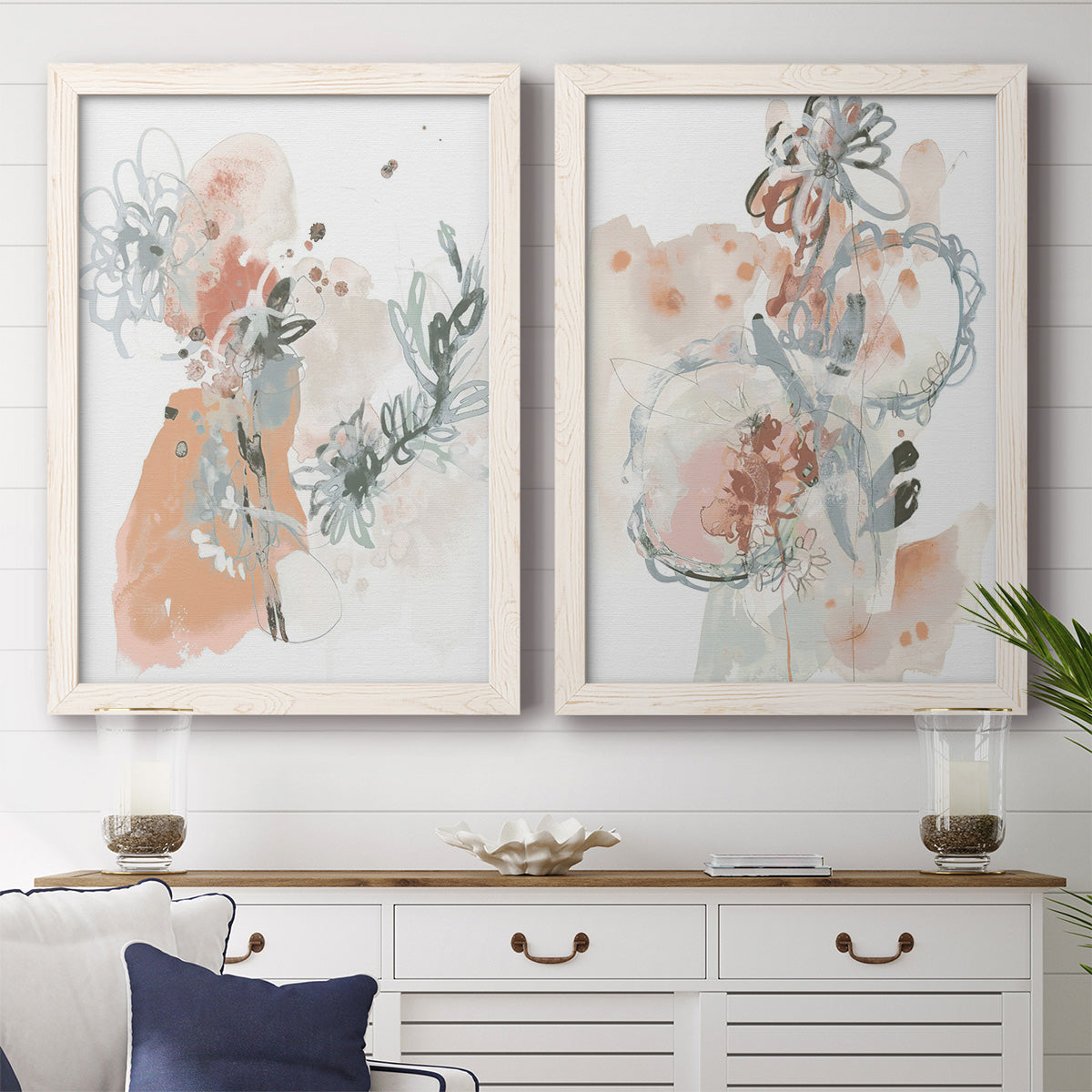Set of two white barnwood framed canvas prints depicting a coordinated art pair of loose blush gray and coral floral gestures rendered as abstract watercolor botanicals above a dining room sideboard.