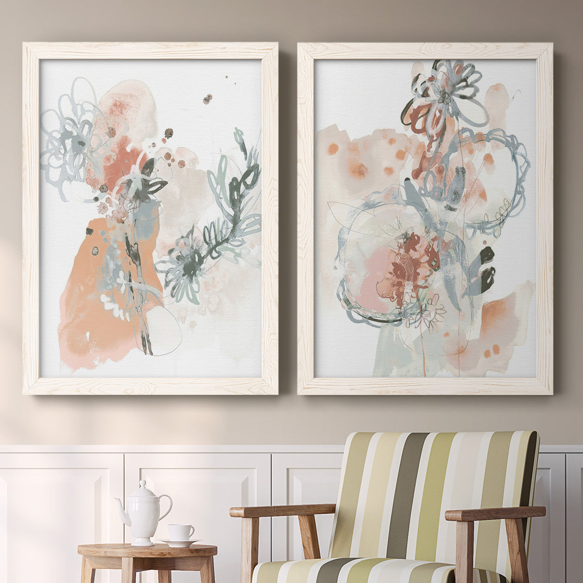 Set of two white barnwood framed canvas prints depicting two abstract watercolor botanicals featuring loose blush gray and coral floral gestures above a sideboard in a cozy sitting room.