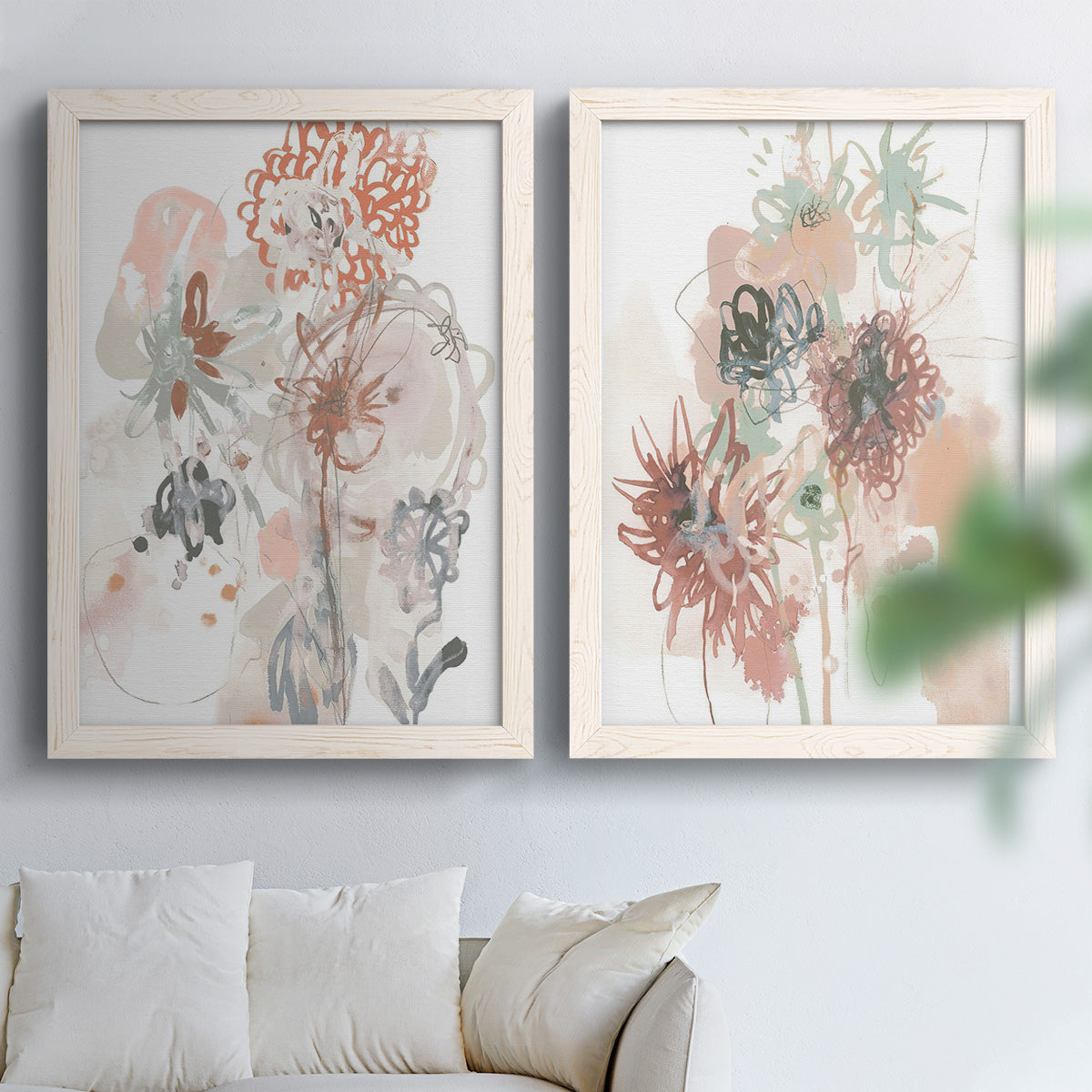 Set of two white barnwood framed canvas prints depicting scribbled petals, translucent washes, and drifting stems arranged across two complementary compositions above a sofa in a bright living space.
