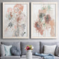 Set of two white barnwood framed canvas prints depicting paired abstract watercolor botanicals with scribbled petals, translucent washes, and drifting stems above a sofa in a contemporary living room.