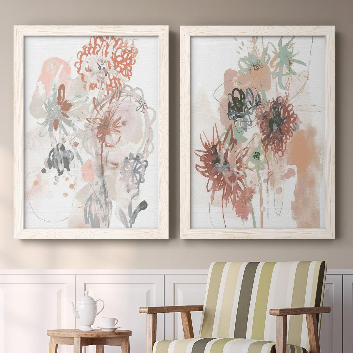 Set of two white barnwood framed canvas prints depicting two abstract watercolor botanicals featuring loose blush gray and coral floral gestures above a sideboard in a cozy sitting room.