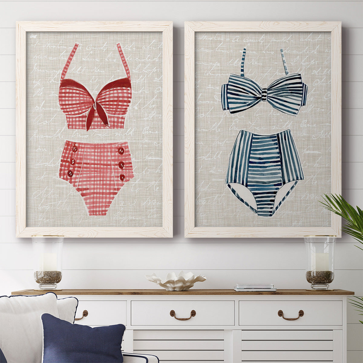 Set of two white barnwood framed canvas prints depicting a coordinated art pair of retro two-piece swimsuits displayed on textured linen grounds rendered as vintage fashion illustrations above a dining room sideboard.