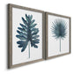 Angled view of a set of two gray barnwood framed canvas prints featuring two modern botanical illustrations featuring large blue-green tropical leaves.