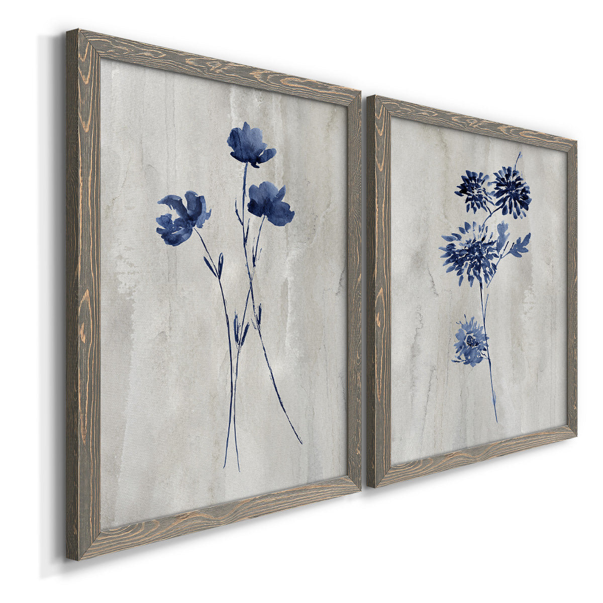 Angled view of a set of two gray barnwood framed canvas prints featuring two rustic monochrome botanical paintings featuring blue wildflower stems on weathered neutral paper.
