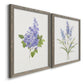 Angled view of a set of two gray barnwood framed canvas prints featuring two delicate watercolor botanical studies featuring purple lilac and blue wildflower stems.