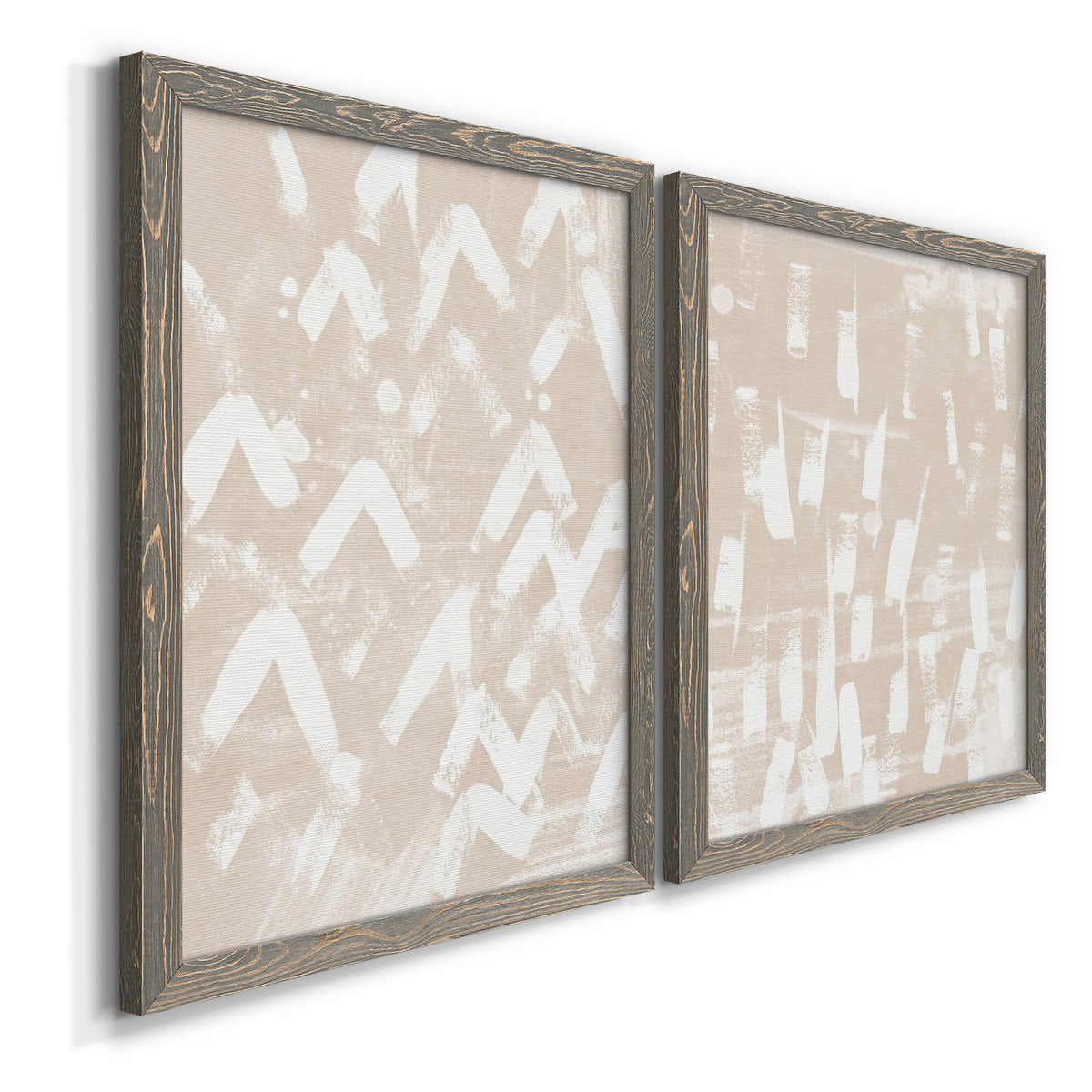 Angled view of a set of two gray barnwood framed canvas prints featuring two tribal-inspired pattern abstracts featuring white hand-painted dashes arcs and chevrons.