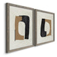 Angled view of a set of two gray barnwood framed canvas prints featuring two minimalist geometric collage abstracts featuring black brown and cream cutout-like forms.