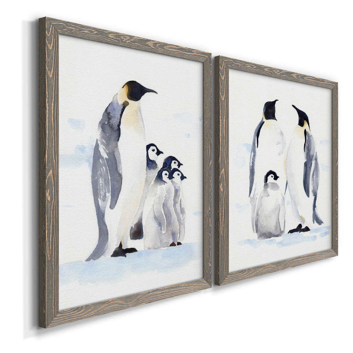 Angled view of a set of two gray barnwood framed canvas prints featuring two soft watercolor wildlife illustrations featuring adult emperor penguins with fluffy chicks.