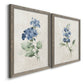 Angled view of a set of two gray barnwood framed canvas prints featuring two farmhouse botanical illustrations featuring blue periwinkle flowers with leafy stems.