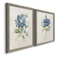 Angled view of a set of two gray barnwood framed canvas prints featuring two farmhouse botanical illustrations featuring blue periwinkle flowers with leafy stems.