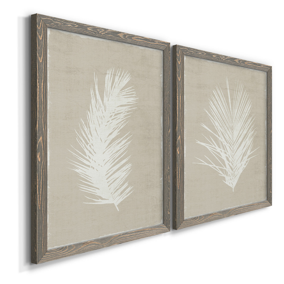 Angled view of a set of two gray barnwood framed canvas prints featuring two minimalist tropical botanical prints featuring white palm frond silhouettes.