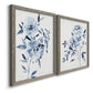Angled view of a set of two gray barnwood framed canvas prints featuring two expressive watercolor botanical paintings featuring loose blue flowers and leafy branches.