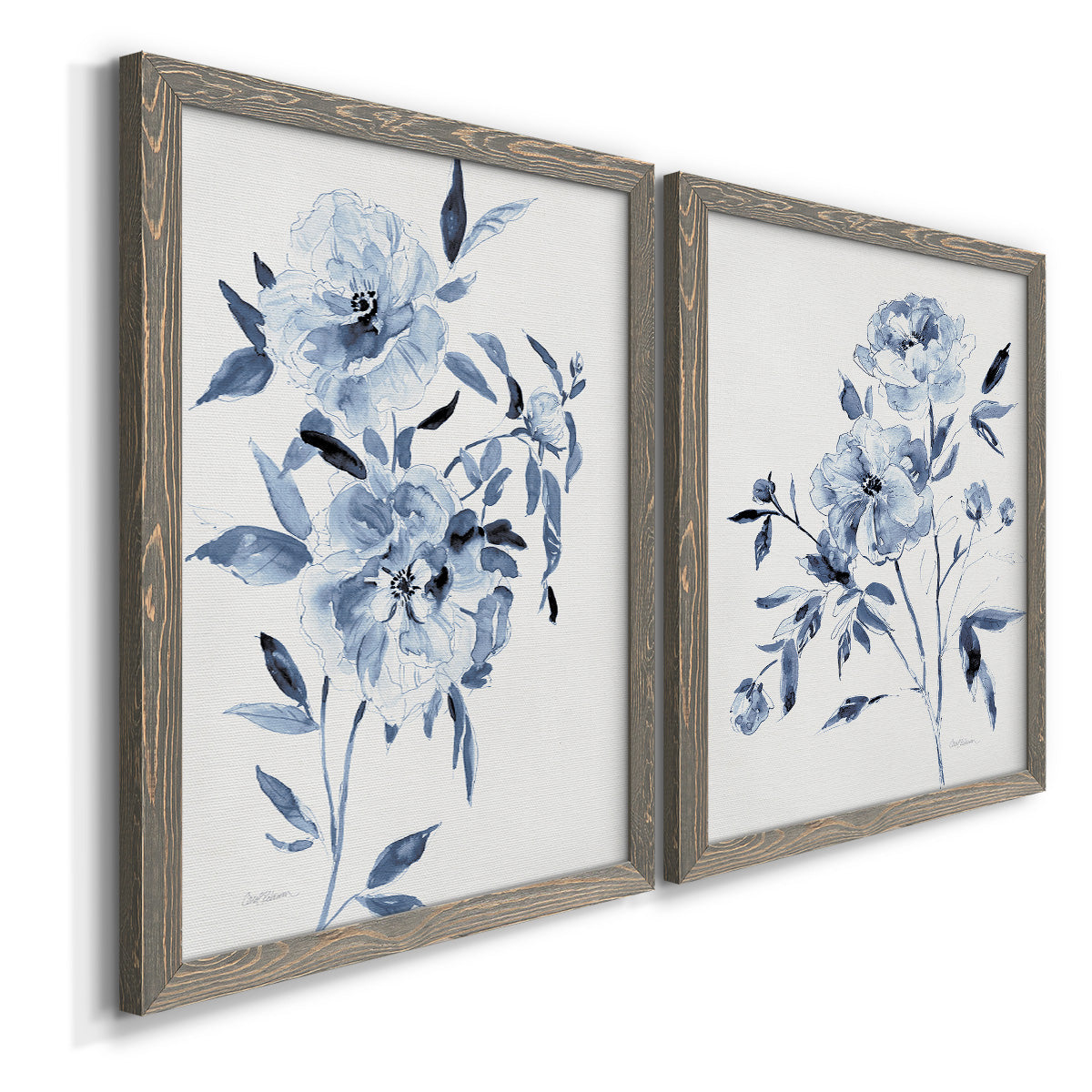 Angled view of a set of two gray barnwood framed canvas prints featuring two expressive watercolor botanical paintings featuring loose blue flowers and leafy branches.