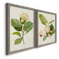 Angled view of a set of two gray barnwood framed canvas prints featuring two traditional botanical paintings featuring white magnolia blossoms and glossy green leaves.