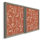 Angled view of a set of two gray barnwood framed canvas prints featuring two graphic portrait patterns featuring many continuous-line faces across terracotta grounds.