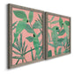 Angled view of a set of two gray barnwood framed canvas prints featuring two bold tropical botanical prints featuring large green tropical leaves on coral-pink grounds.