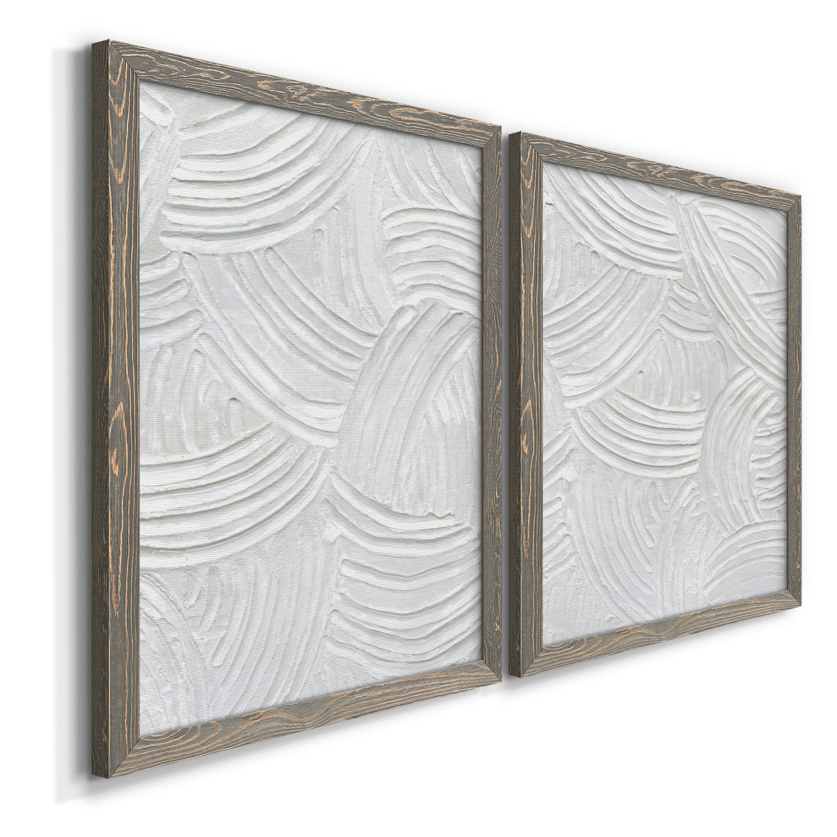 Angled view of a set of two gray barnwood framed canvas prints featuring two textural monochrome abstracts featuring overlapping white carved arcs and ridges.