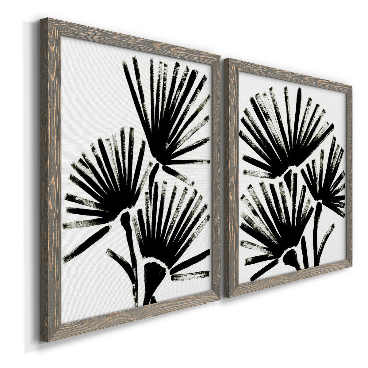 Angled view of a set of two gray barnwood framed canvas prints featuring two bold monochrome botanical prints featuring black fan-shaped botanical forms.