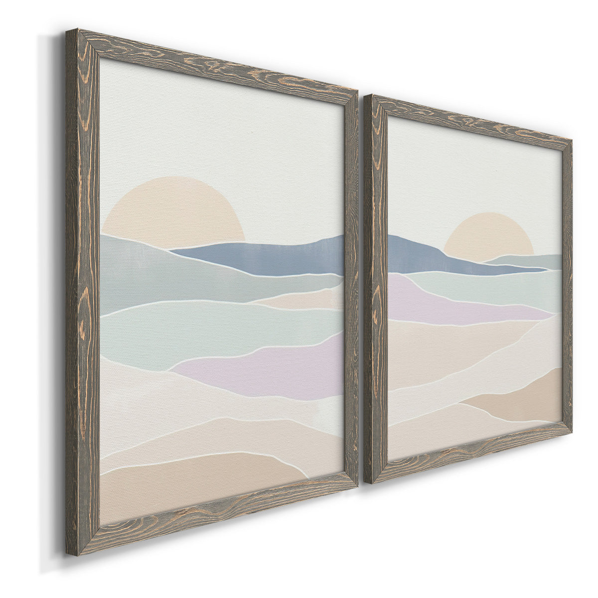 Angled view of a set of two gray barnwood framed canvas prints featuring two minimalist abstract landscapes featuring layered pastel waves beneath a pale setting sun.