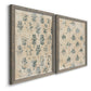Angled view of a set of two gray barnwood framed canvas prints featuring two weathered block-print patterns featuring small repeating blue floral motifs.