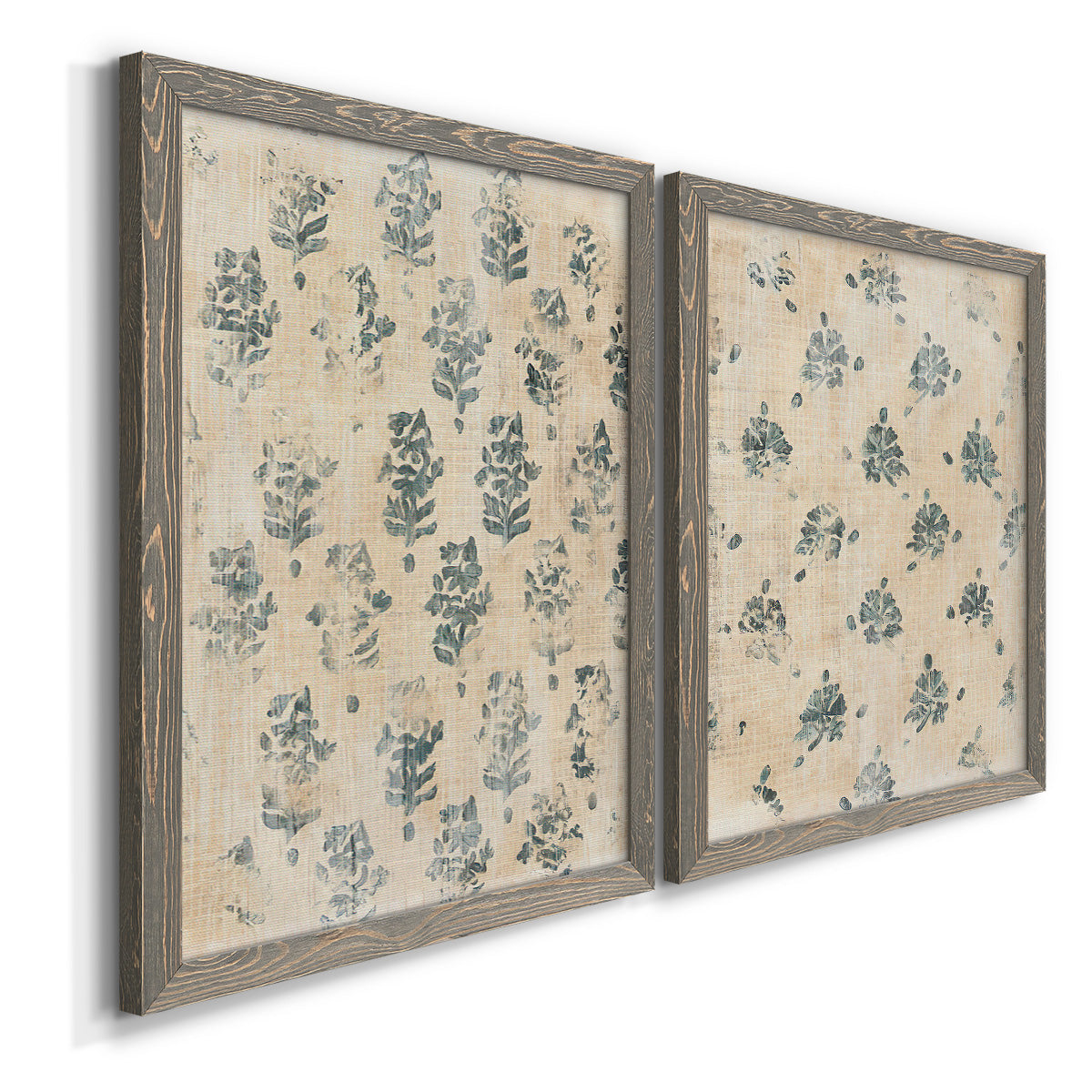Angled view of a set of two gray barnwood framed canvas prints featuring two weathered block-print patterns featuring small repeating blue floral motifs.