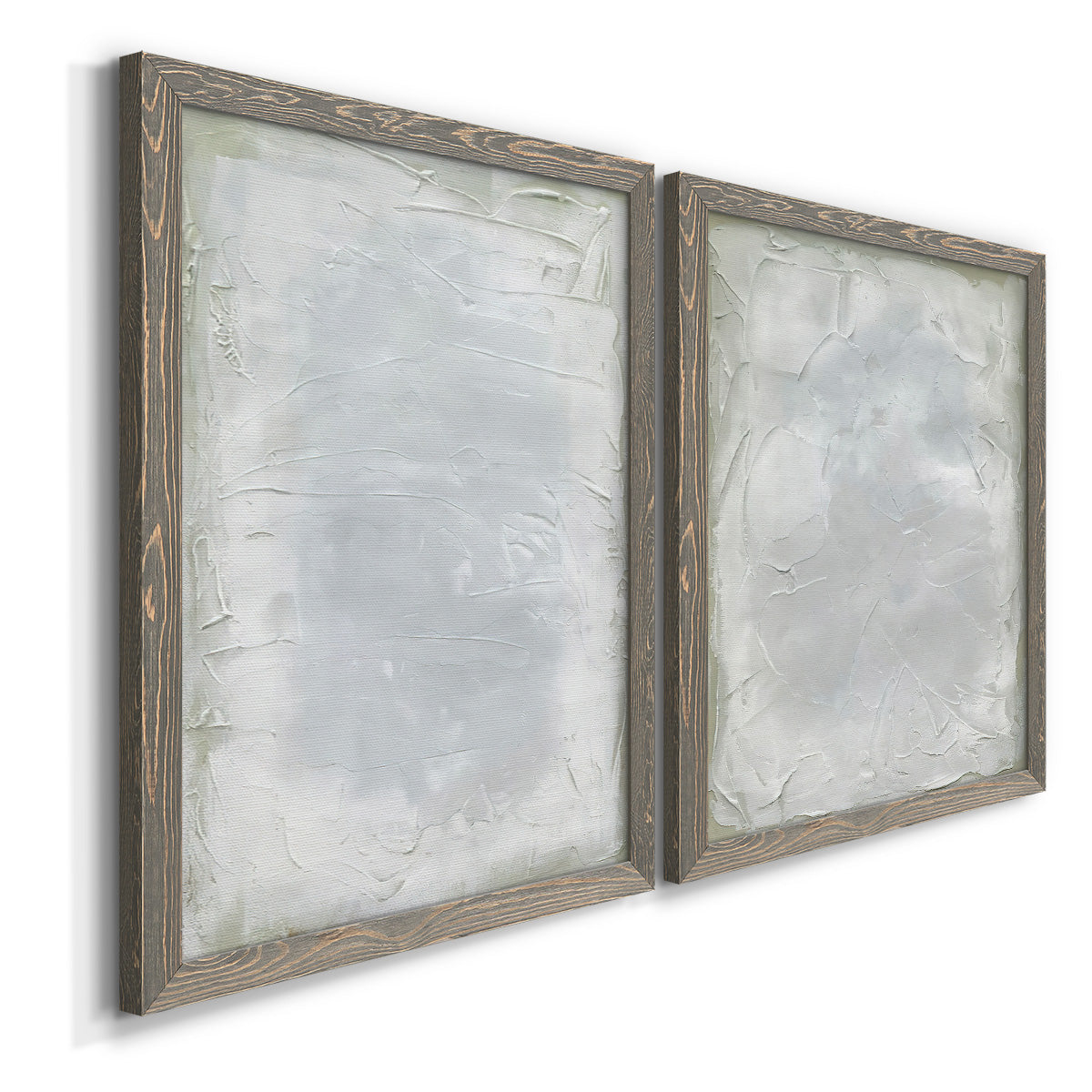 Angled view of a set of two gray barnwood framed canvas prints featuring two quiet textural abstracts featuring layered white and silver-gray painted surfaces.