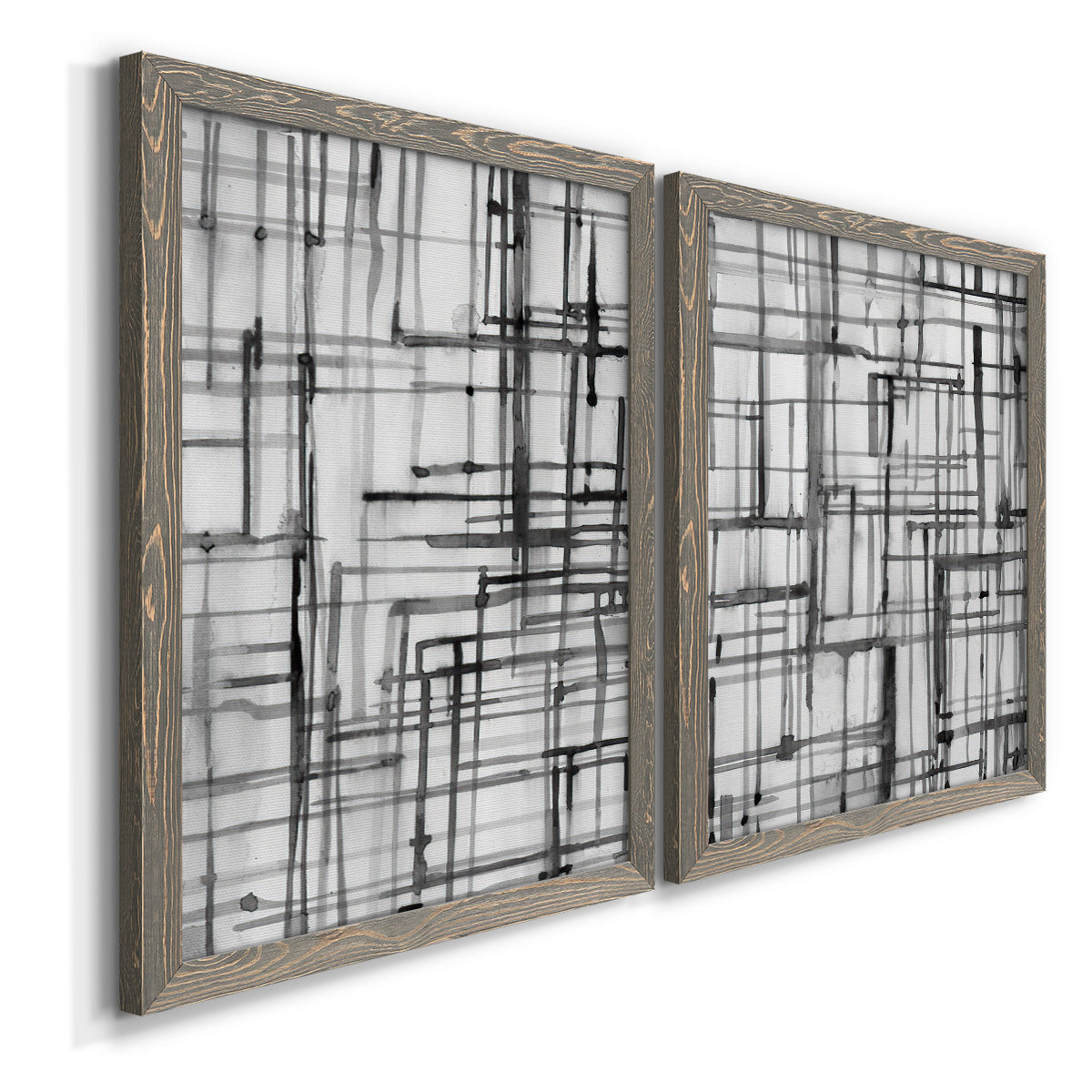 Angled view of a set of two gray barnwood framed canvas prints featuring two monochrome geometric abstracts featuring layered black linear grids.
