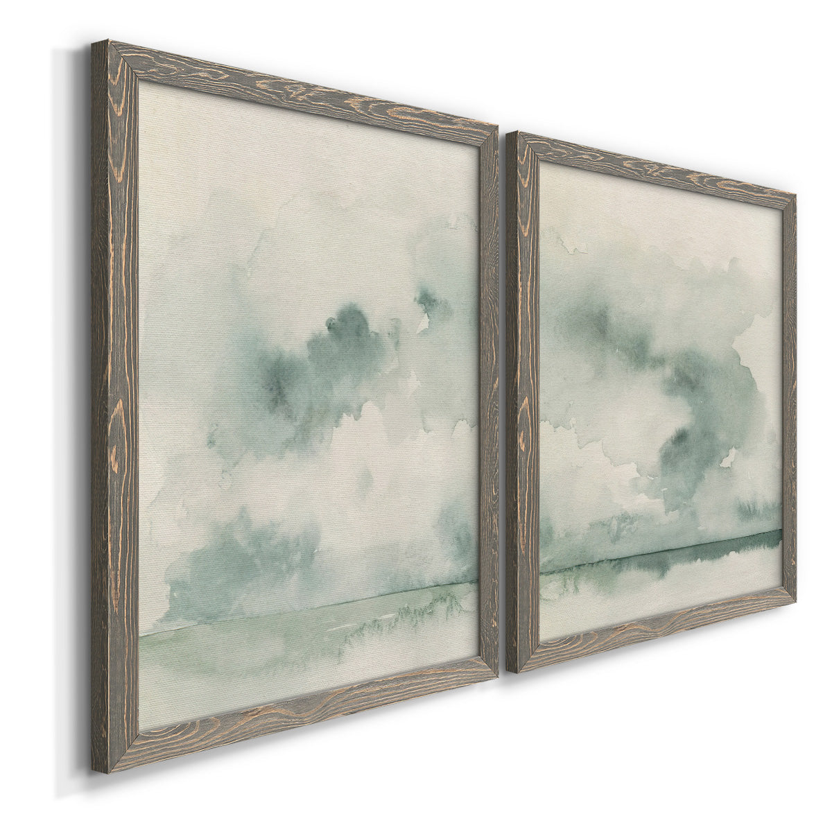 Angled view of a set of two gray barnwood framed canvas prints featuring two minimalist watercolor seascapes with misty green clouds calm horizons and pale reflective water.