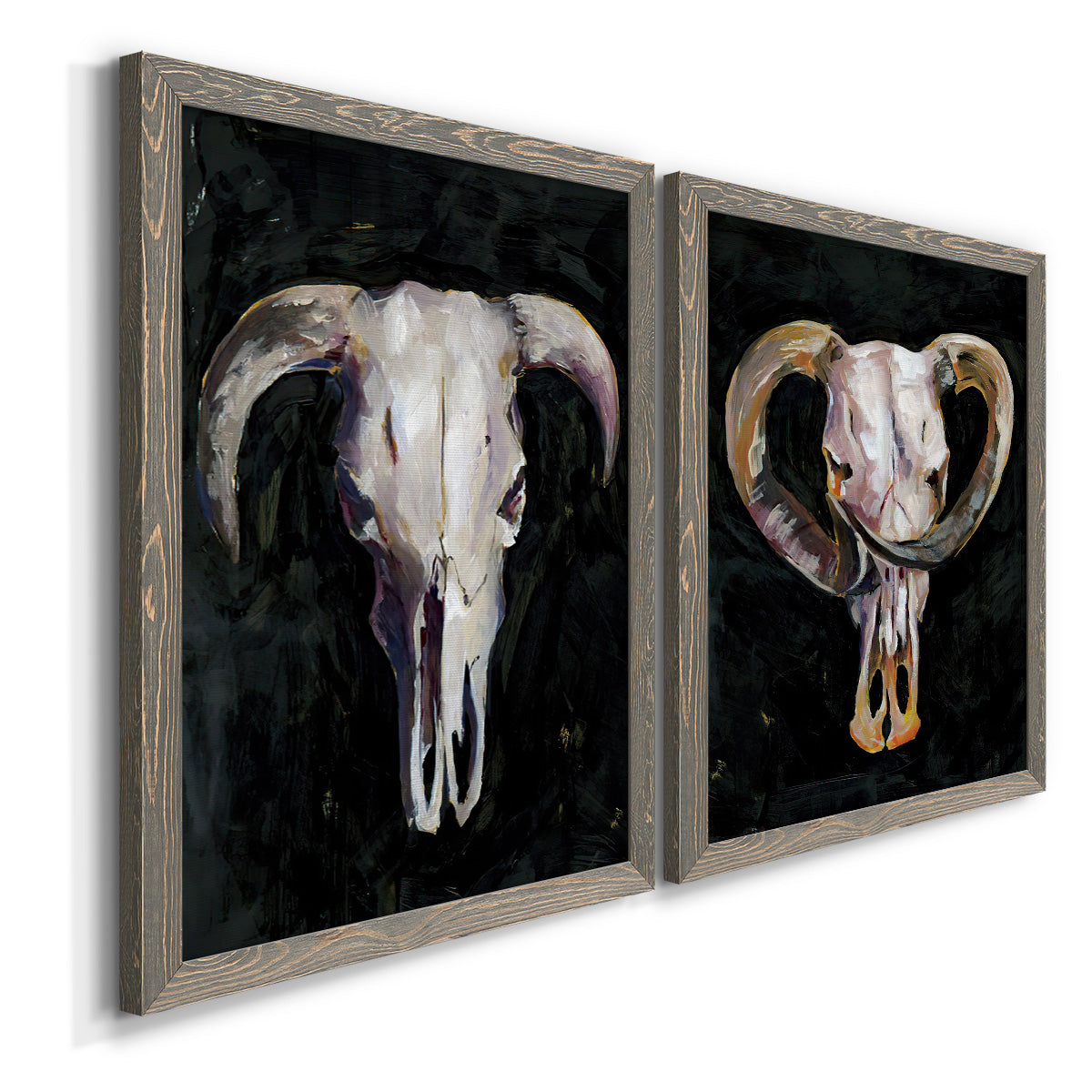 Angled view of a set of two gray barnwood framed canvas prints featuring two dramatic Western animal paintings featuring ram and cattle skulls against black grounds.