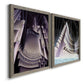 Angled view of a set of two gray barnwood framed canvas prints featuring two vintage architectural illustrations featuring dramatic Art Deco city and theater scenes.