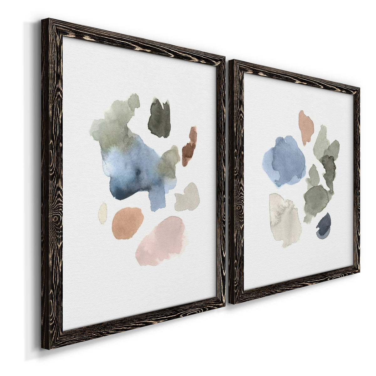 Angled view of a set of two black barnwood framed canvas prints featuring two airy minimalist abstracts featuring scattered translucent watercolor shapes.