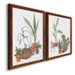 Angled view of a set of two maple barnwood framed canvas prints featuring two whimsical botanical animal illustrations featuring cats tucked among collections of potted houseplants.