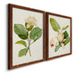 Angled view of a set of two maple barnwood framed canvas prints featuring two traditional botanical paintings featuring white magnolia blossoms and glossy green leaves.