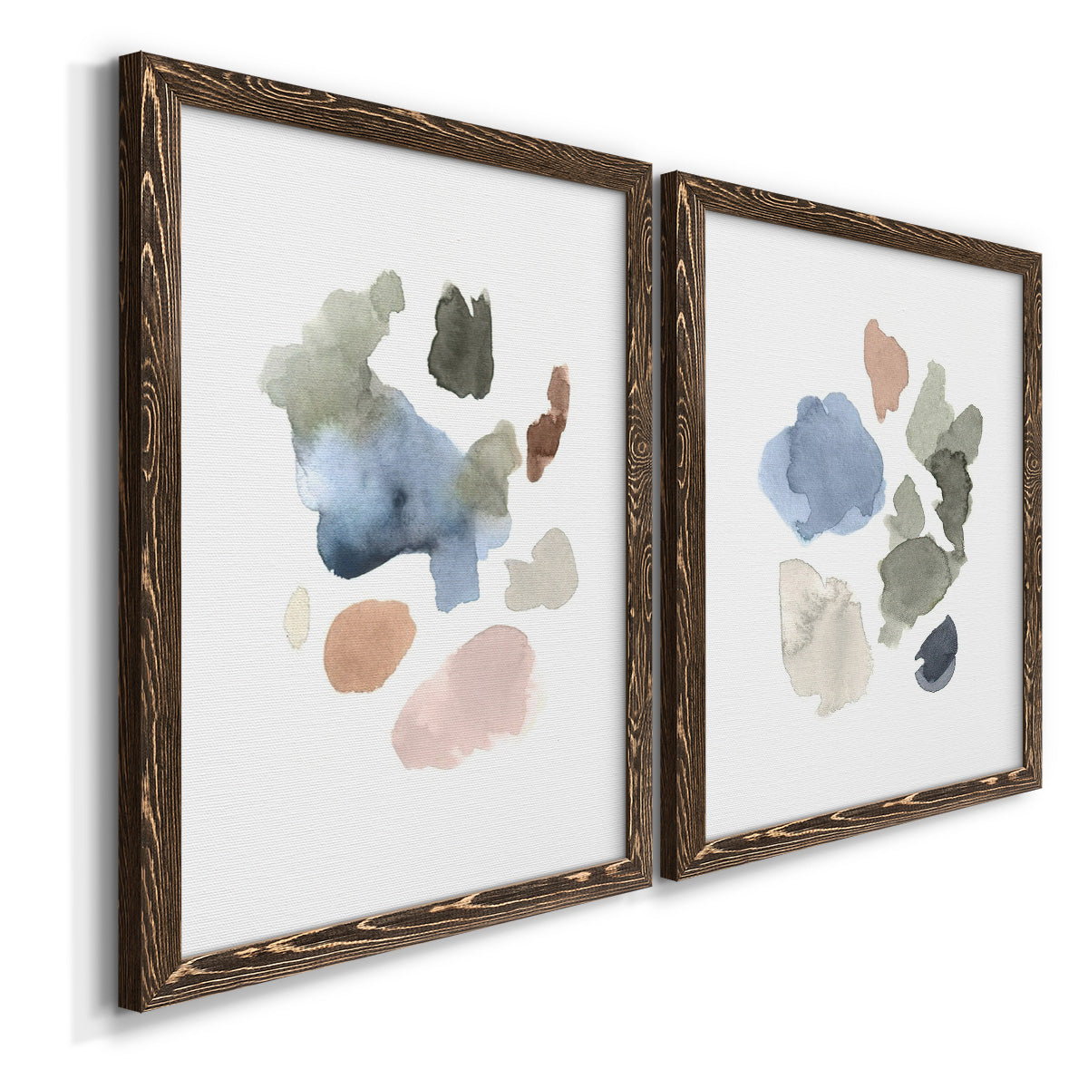 Angled view of a set of two walnut barnwood framed canvas prints featuring two airy minimalist abstracts featuring scattered translucent watercolor shapes.