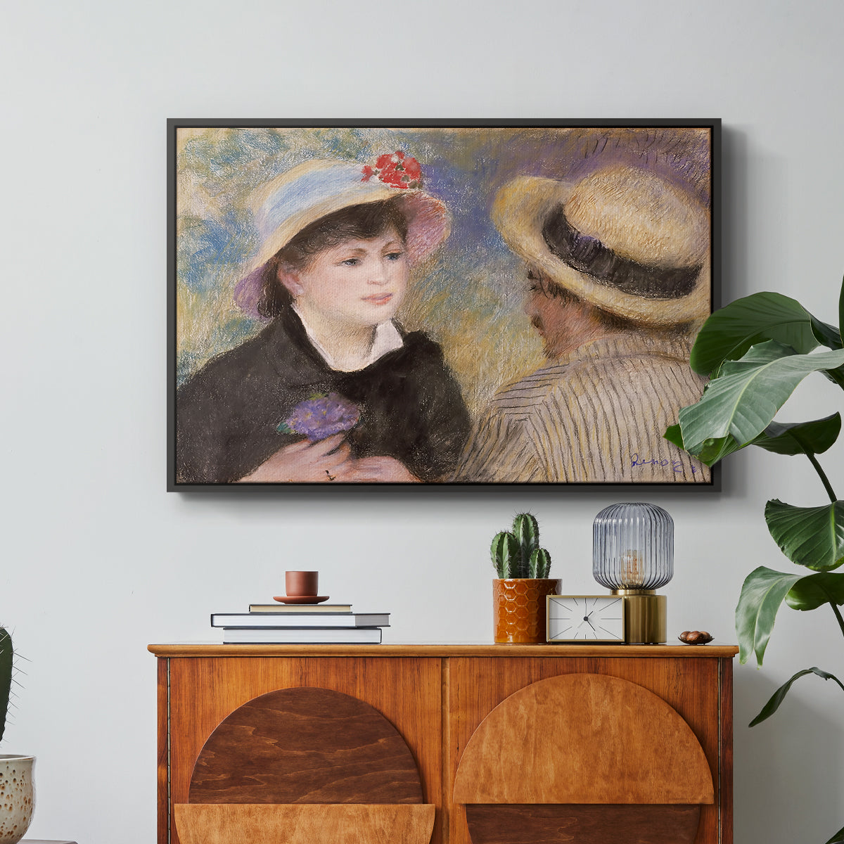 Boating Couple (Aline Charigot and Renoir), c. 1881 by Pierre-Auguste Renoir in a black floater framed canvas featuring a close-up of a couple seated together outdoors with hats and soft sunlight, displayed above a wood console cabinet.