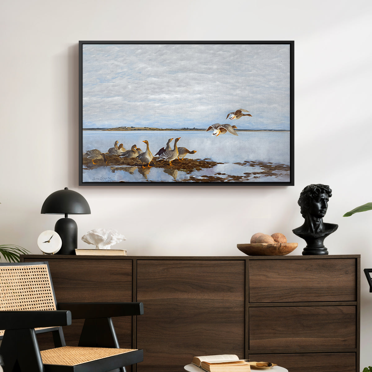 Greylag Geese (Grågäss), 1922 by Bruno Liljefors displayed in a black floater framed canvas above a dark wood credenza in an entryway.