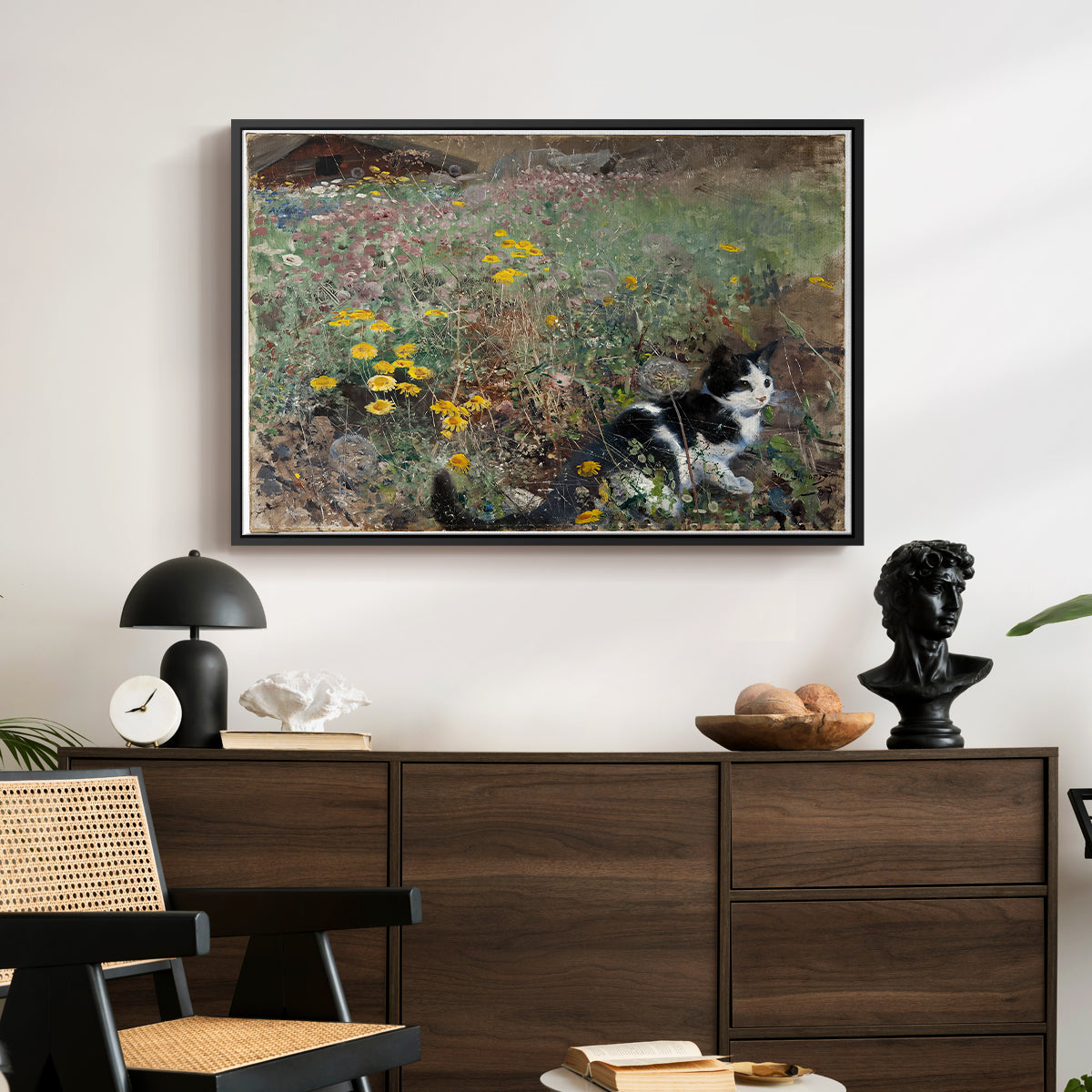 Cat on a Flowery Meadow, 1887 by Bruno Liljefors displayed in a black floater framed canvas above a dark wood credenza in an entryway.