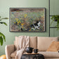 Black floater framed canvas featuring a naturalistic depiction of cat in blooming countryside setting, displayed above a sofa in a modern living room.