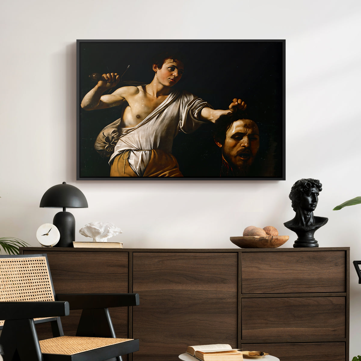 David with the Head of Goliath (Vienna Version), c. 1607 by Caravaggio displayed in a black floater framed canvas above a dark wood credenza in an entryway.