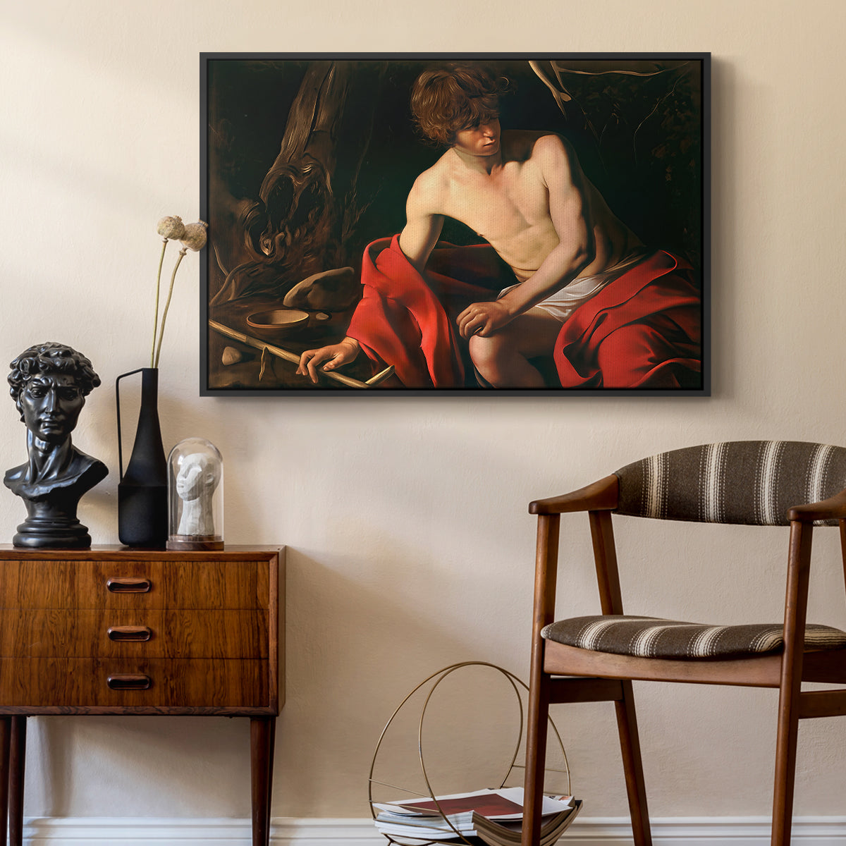 Saint John the Baptist in the Wilderness, c. 1603-1604 by Caravaggio as a black floater framed canvas featuring a biblical youth seated outdoors with symbolic staff and minimal landscape, styled above a mid-century console in a contemporary living area.