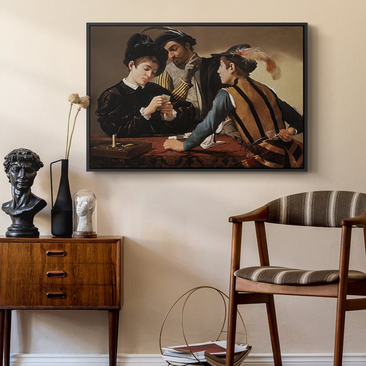 The Cardsharps, c. 1594 by Caravaggio as a black floater framed canvas featuring a young men playing cards with one cheating and another watching closely, styled above a mid-century console in a contemporary living area.