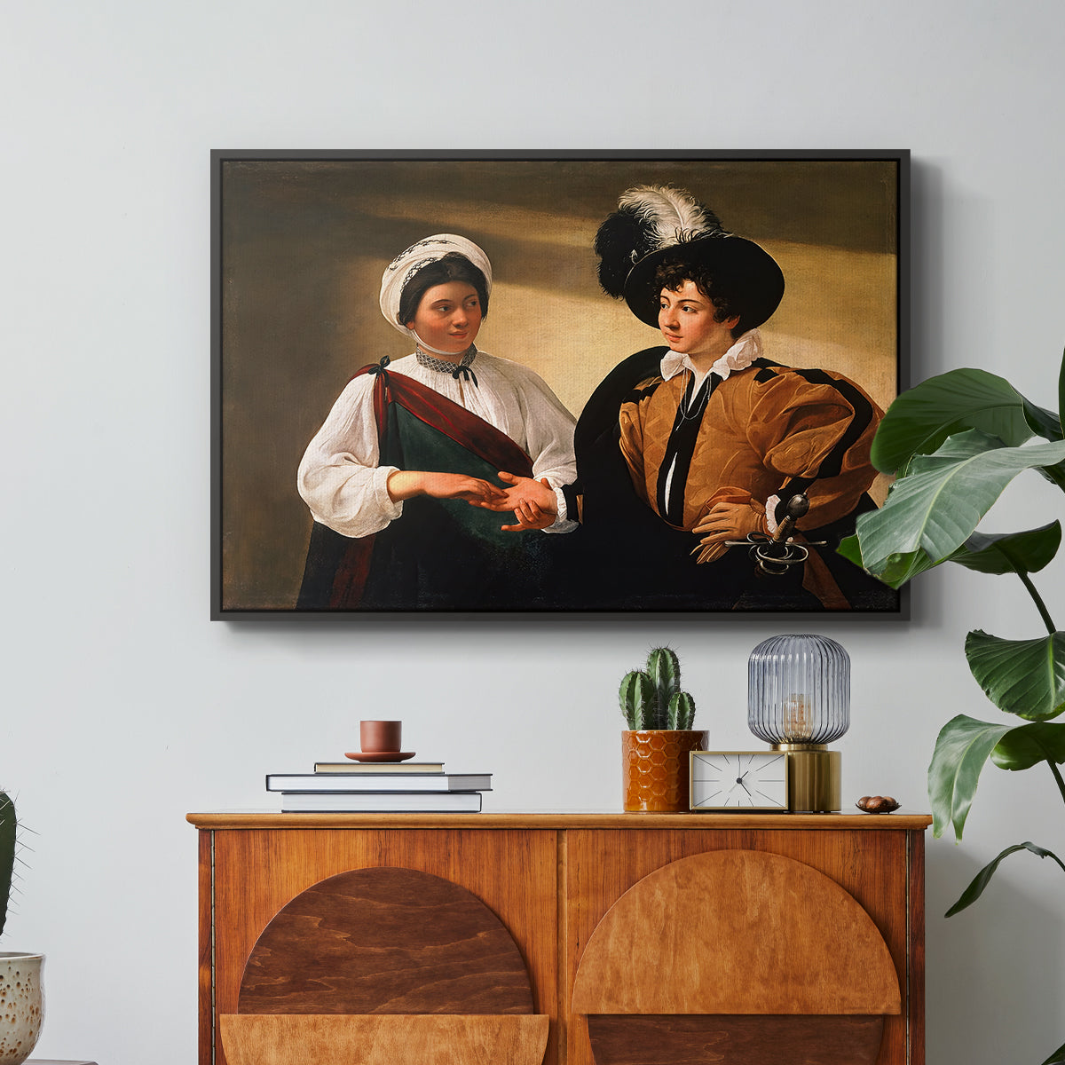 The Fortune Teller (Louvre Version), c. 1595 by Caravaggio in a black floater framed canvas featuring a woman reading a young man's palm while secretly stealing his ring, displayed above a wood console cabinet.