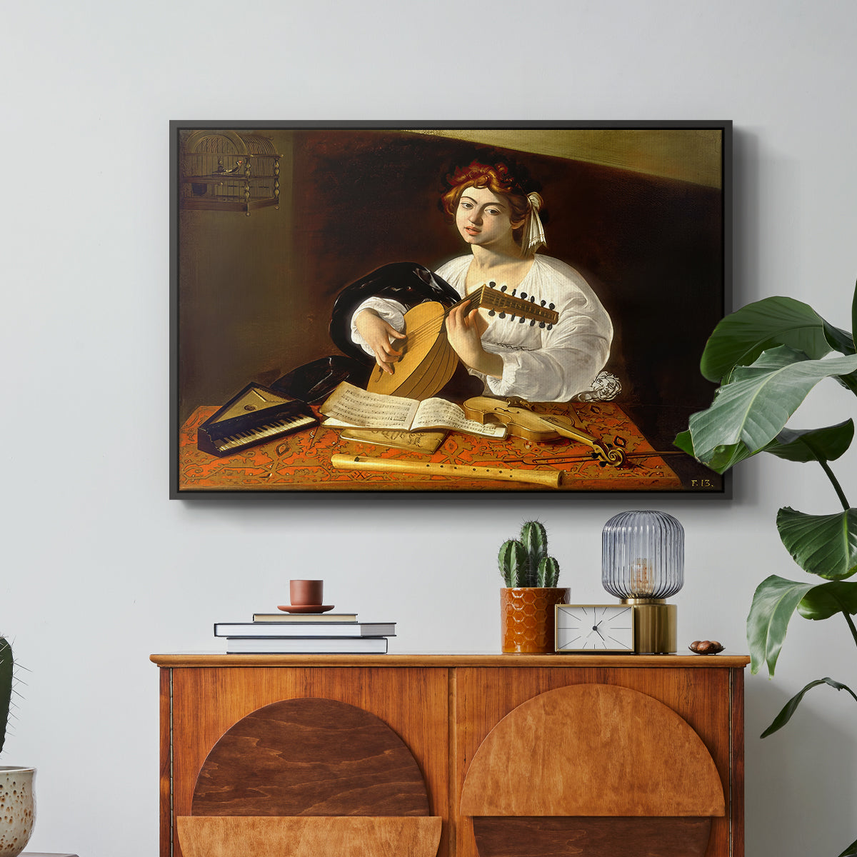The Lute Player (Wildenstein Version), c. 1596 by Caravaggio in a black floater framed canvas featuring a young man playing lute surrounded by sheet music and still life objects, displayed above a wood console cabinet.