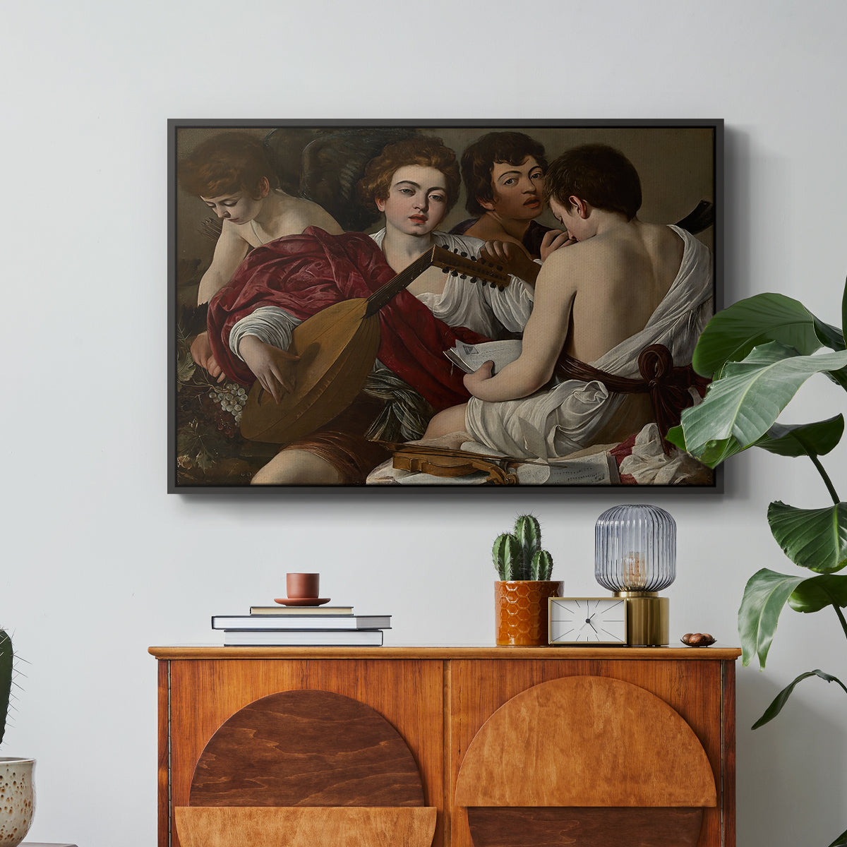 The Musicians, c. 1595 by Caravaggio in a black floater framed canvas featuring a group of young men gathered together playing music with instruments, displayed above a wood console cabinet.