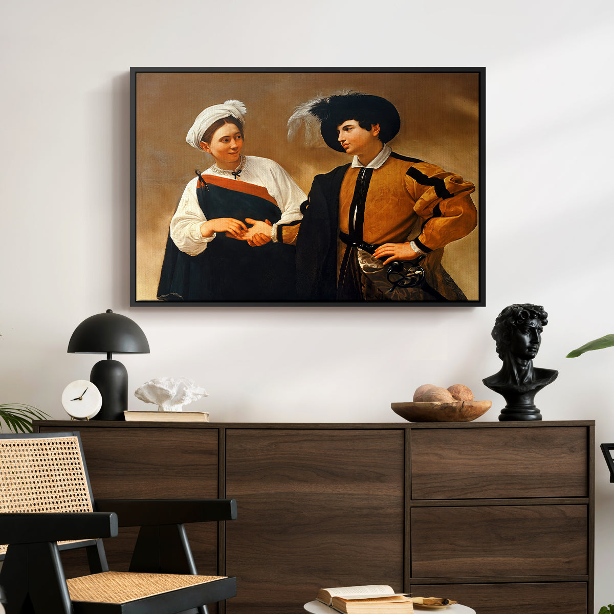 The Fortune Teller (Capitoline Version), c. 1599 by Caravaggio displayed in a black floater framed canvas above a dark wood credenza in an entryway.