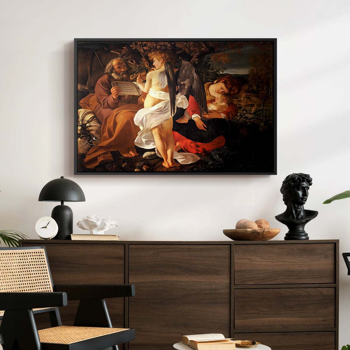 Rest on the Flight into Egypt, c. 1597 by Caravaggio displayed in a black floater framed canvas above a dark wood credenza in an entryway.